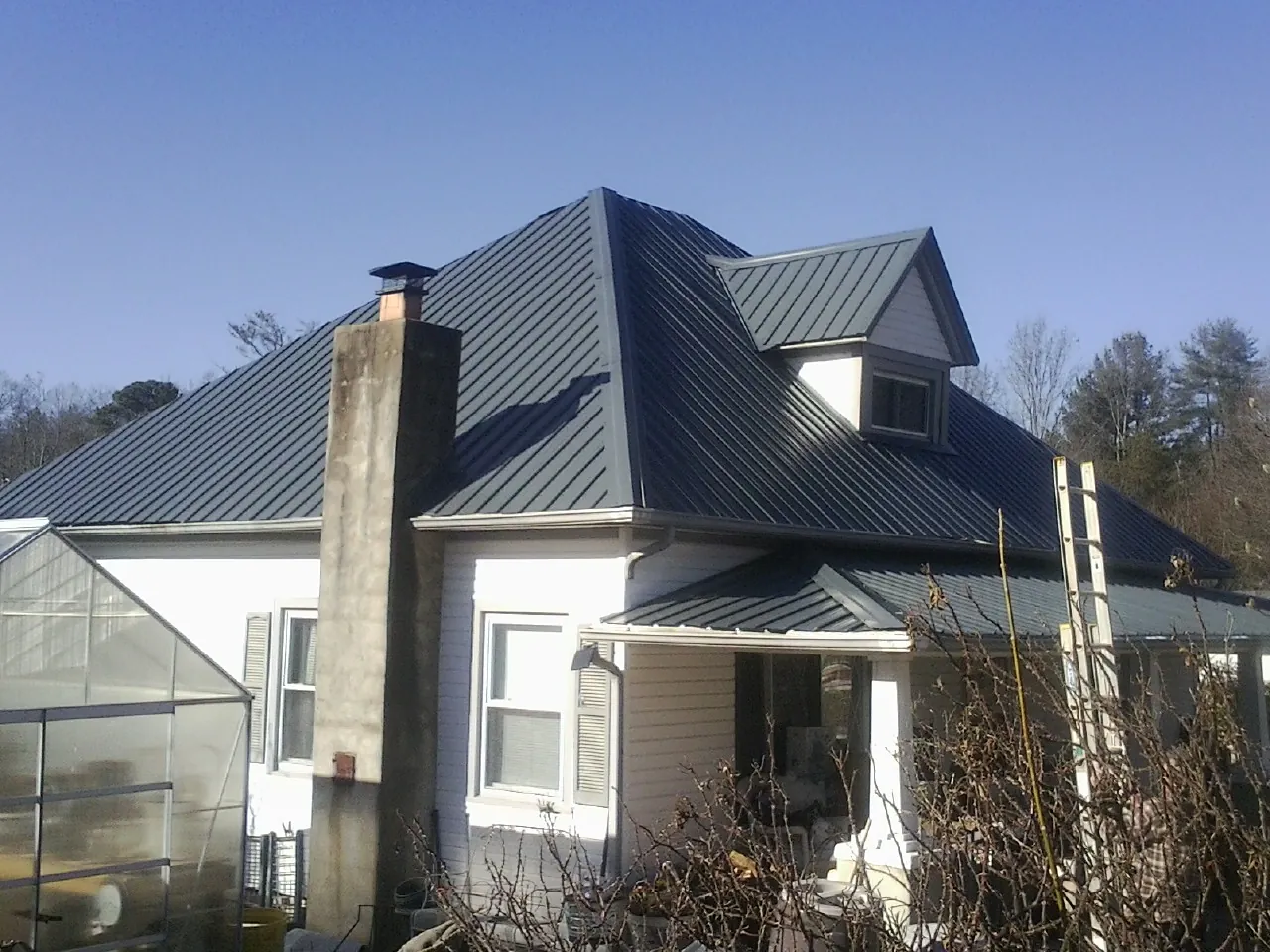 Dark blue standing seam metal roof on a white farmhouse with dormer — Slate & Tile Roof Repair by Roofing Brothers in Guide Rock