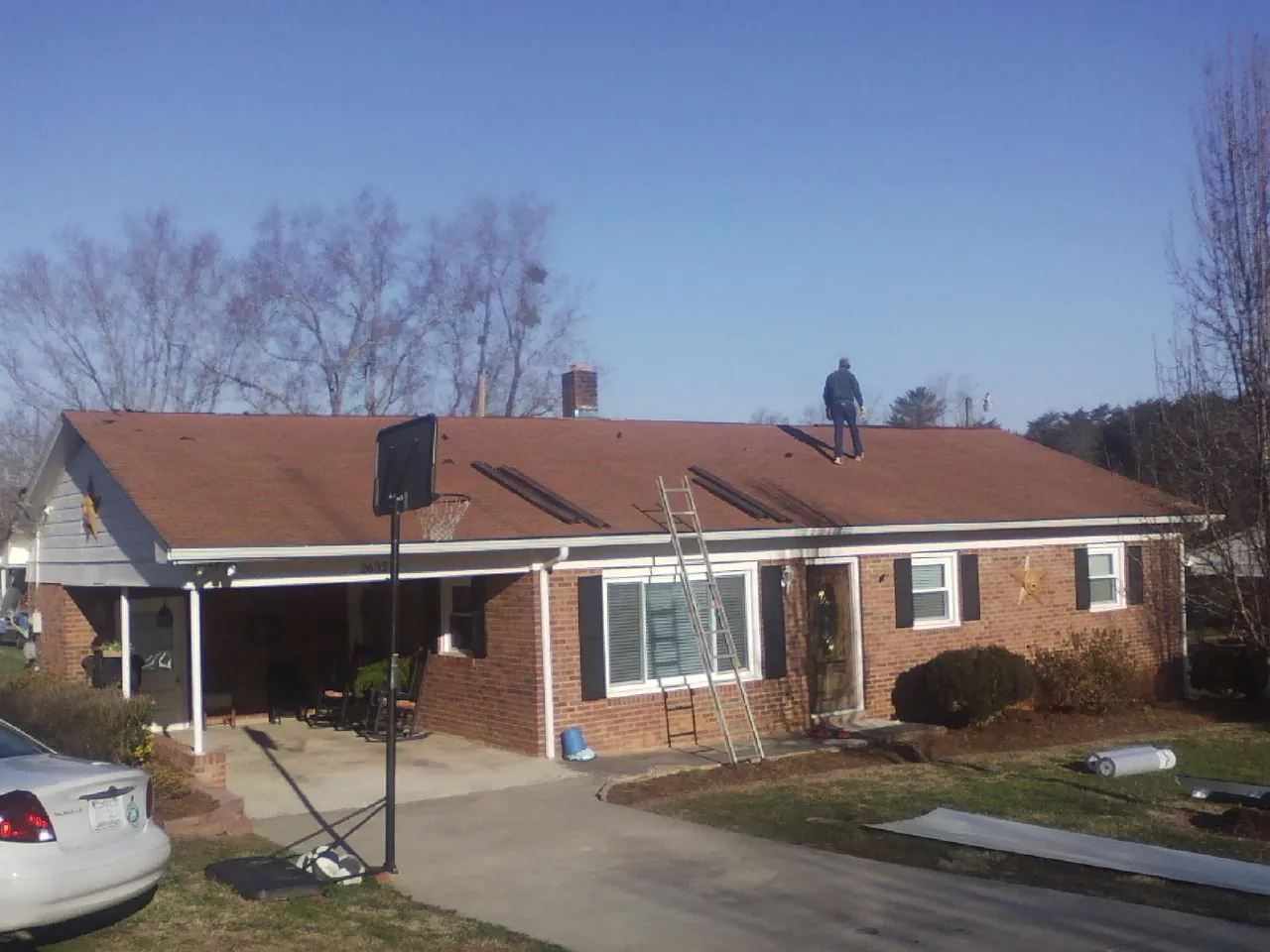 Roofer stripping a shingle roof on a brick ranch before metal panels in Guide Rock