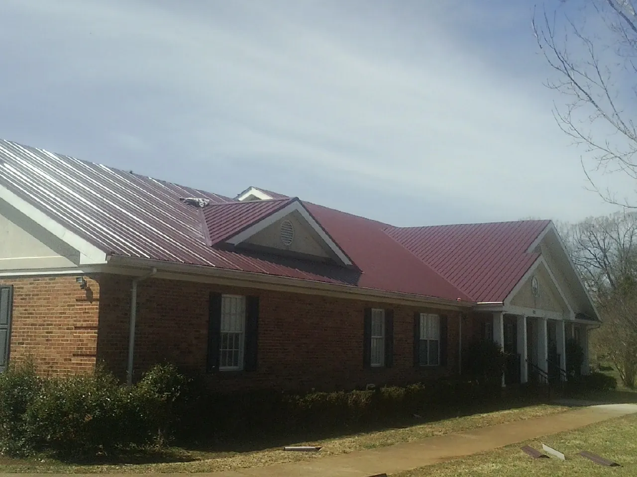 Red metal roof with gabled entries on a long brick building, from a Hail Damage Roof Repair job in Guide Rock