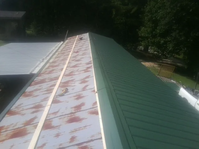 Old rusted panels beside newly installed green metal roofing — Wind Damage Roof Repair by Roofing Brothers in Guide Rock