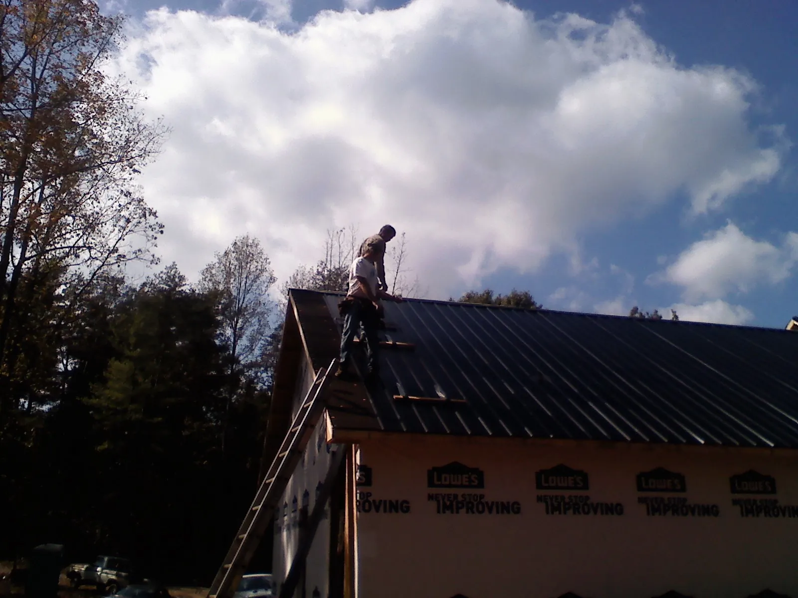 Roofer fastening dark metal panels high against a cloudy sky, from a Roof Inspection job in Guide Rock