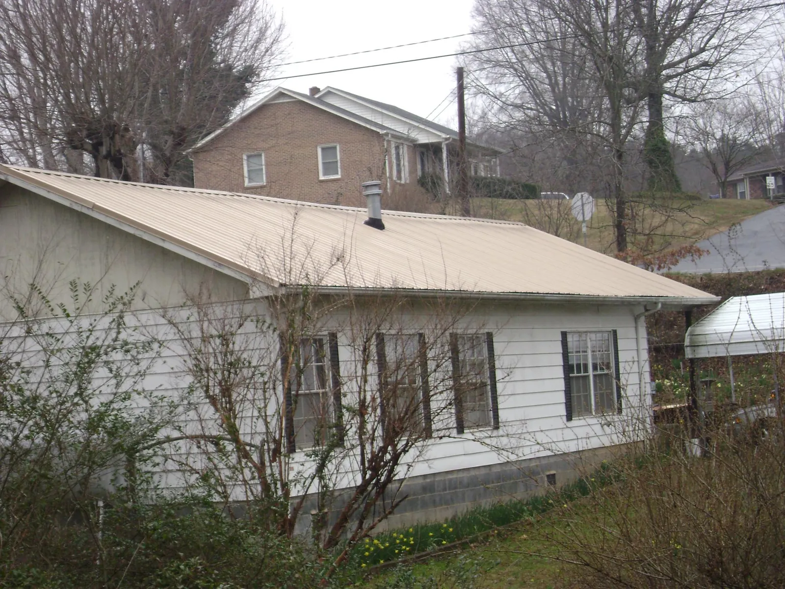 Tan metal roof on a white sided house set into a hillside — Commercial Roofing by Roofing Brothers in Guide Rock