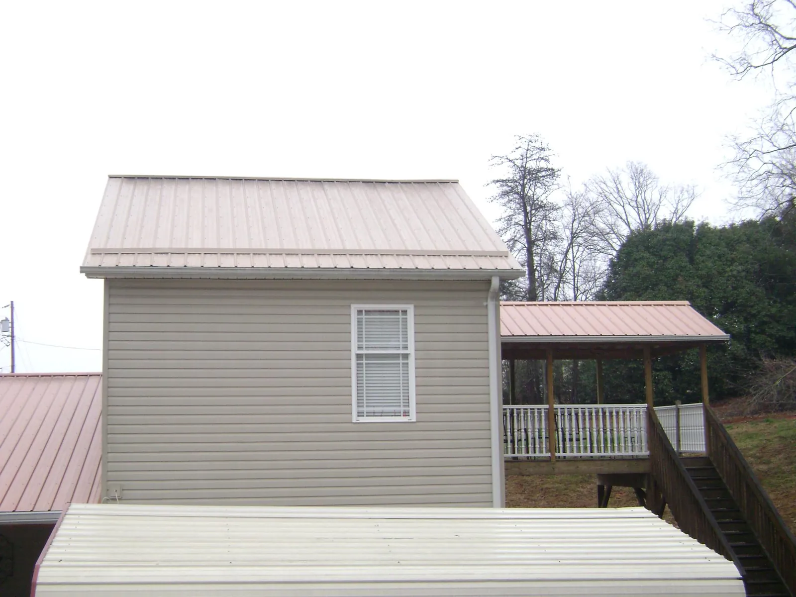Tan metal roofs on a two story addition and attached porch, from a Roof Replacement job in Guide Rock