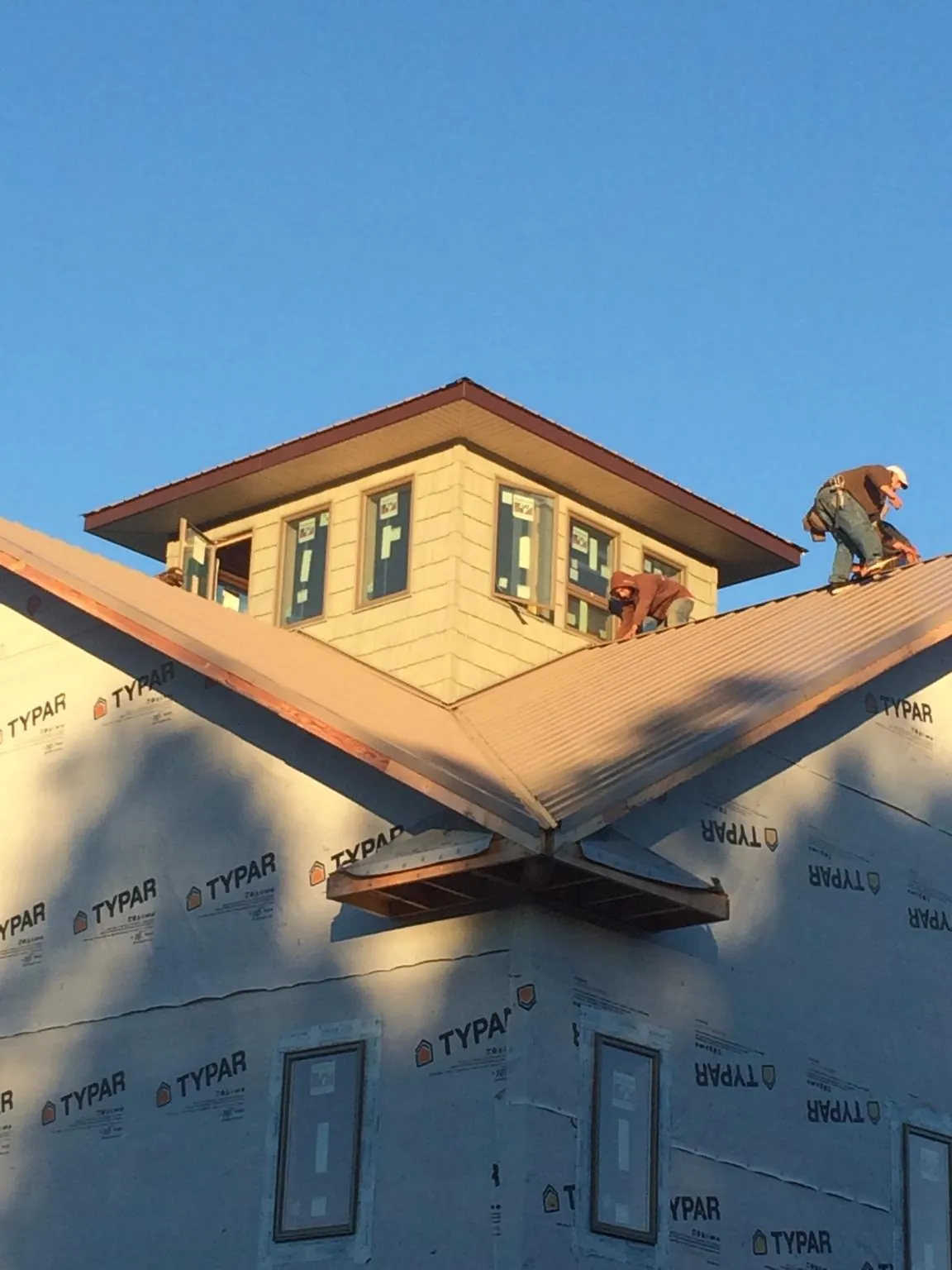 Roofers working around a rooftop cupola on a new metal roof at sunset — Roof Waterproofing in Guide Rock by Roofing Brothers
